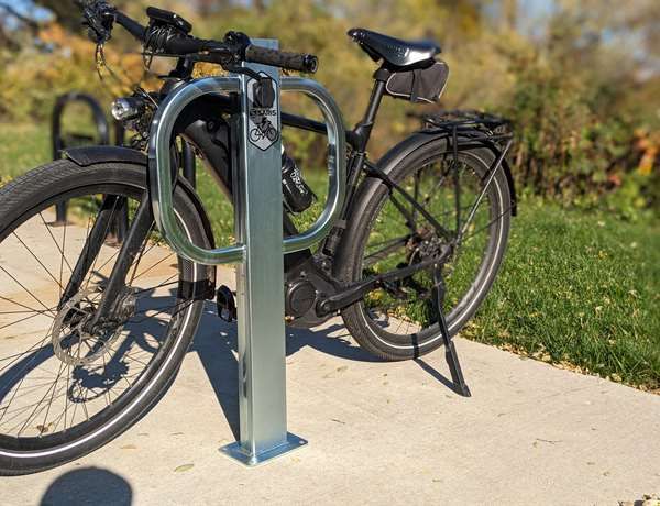 En svart elcykel parkerad vid en laddstolpe utomhus på en betonggång.
