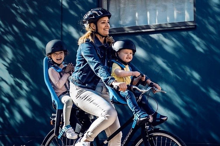 Vuxen cyklar med två hjälmförsedda barn på en familjecykel