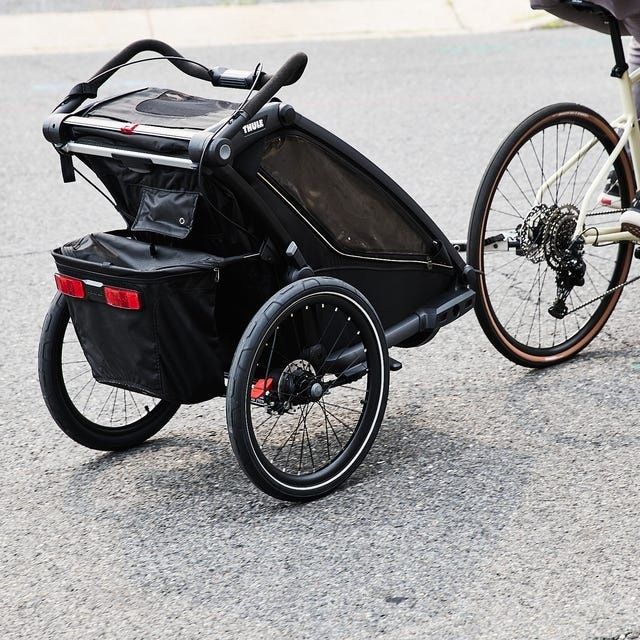 Svart cykelvagn kopplad till en cykel på en asfalterad väg